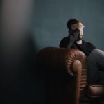 Mental Health - a man holds his head while sitting on a sofa