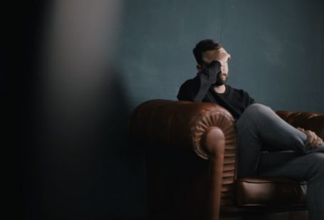 Mental Health - a man holds his head while sitting on a sofa