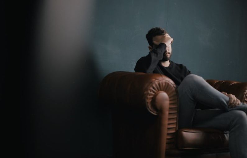Mental Health - a man holds his head while sitting on a sofa