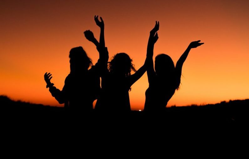 Travel Pets - silhouette of three woman with hands on the air while dancing during sunset